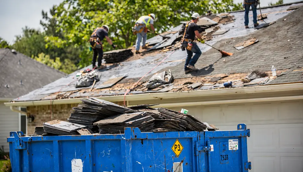 Roofing contractors loading debris into a roll-off dumpster